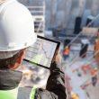 homme qui regarde une tablette devant un chantier BTP