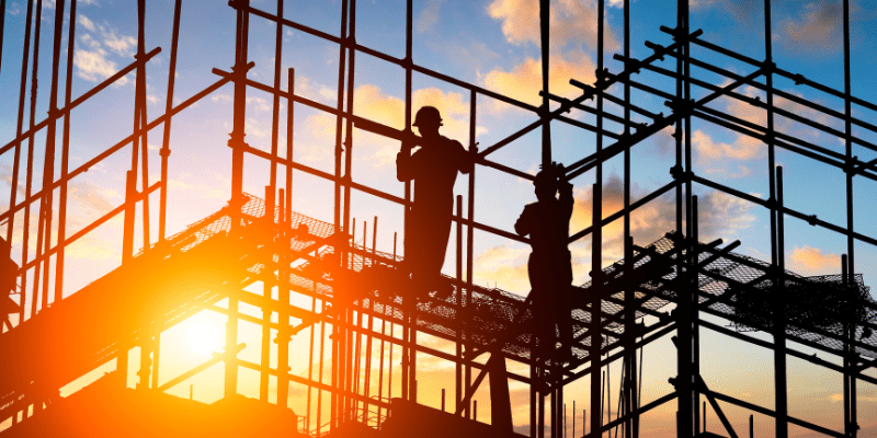Silhouettes de travailleurs de chantier sur un échafaudage au milieu d’une installation de chantier.