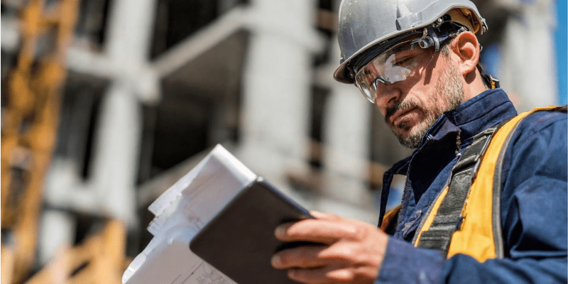Chef de chantier, casqué et équipé, qui vérifie ses documents sur tablette lors de la réception des travaux.