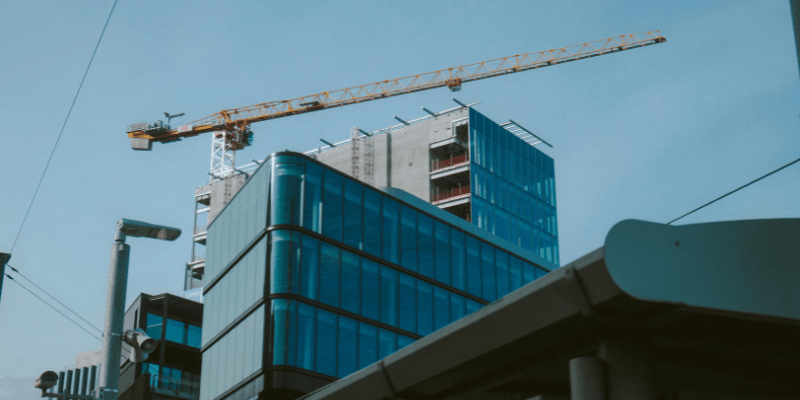 Bâtiment moderne à structure vitrée en cours de construction avec grue de levage.