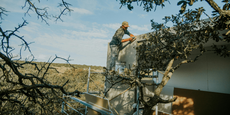 Artisan installant des panneaux sur une structure de bâtiment en bois entourée d'arbres.