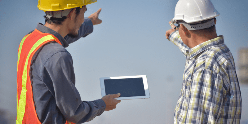 Chef de chantier et responsable terrain consultant une tablette numérique sur un chantier de construction