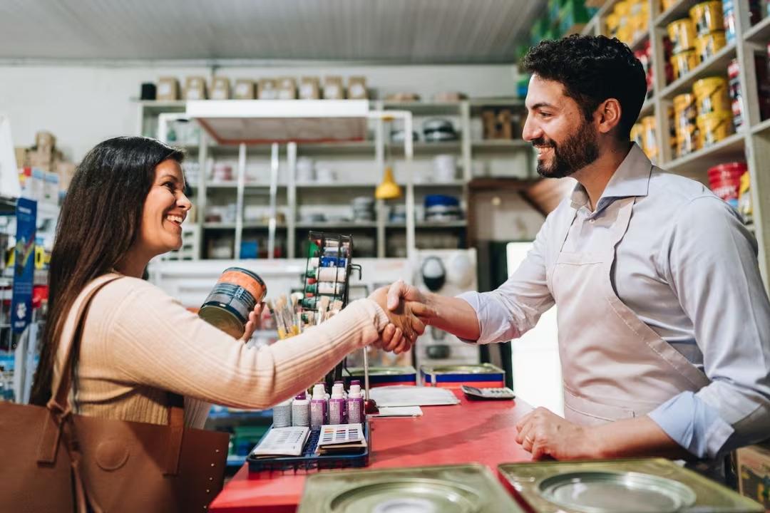 Vendeur de négoce en bâtiment souriant serrant la main d'une cliente dans un magasin de matériaux.