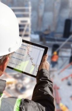 homme qui regarde une tablette devant un chantier BTP